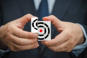 Hände halten zusammengesetzte Würfel mit Zielsymbol als Symbol für Strategie und Fokus